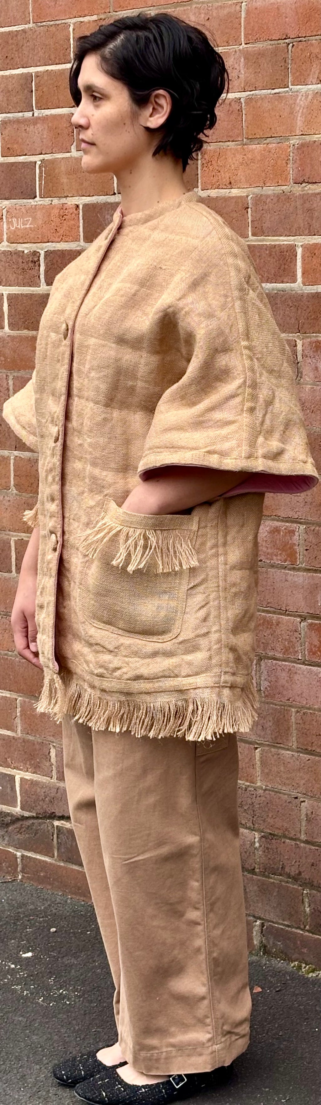 Woman wearing a beige outfit with a textured pattern against a brick wall.