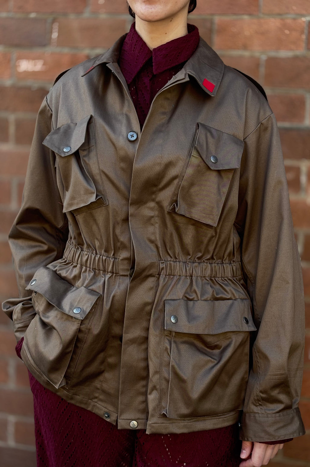 Person wearing a brown jacket with a red label against a brick wall