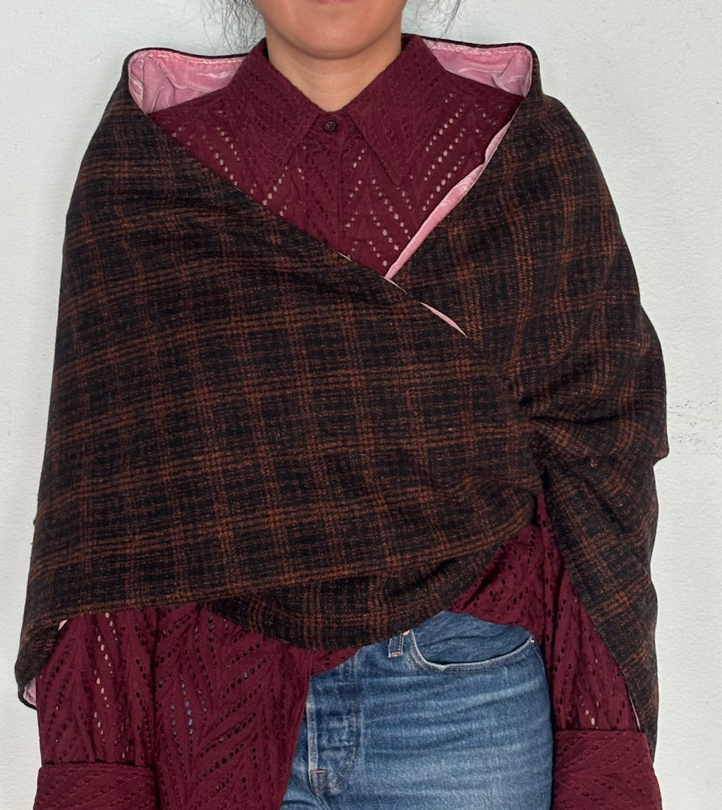 Person wearing a brown plaid shawl over a burgundy garment with a white background