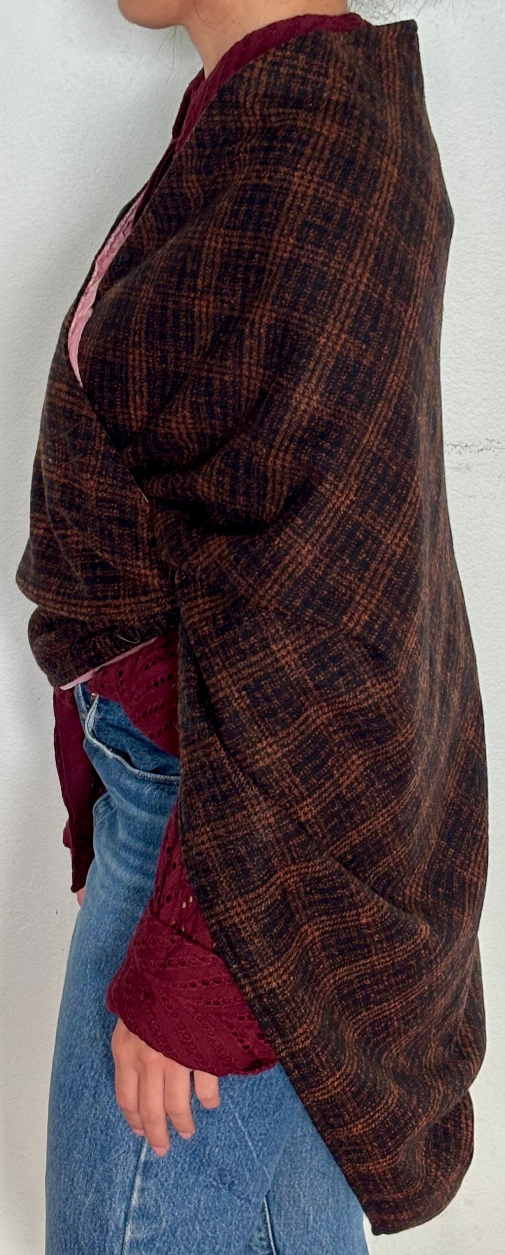 Person wearing a plaid shawl over a red shirt and blue jeans against a white background