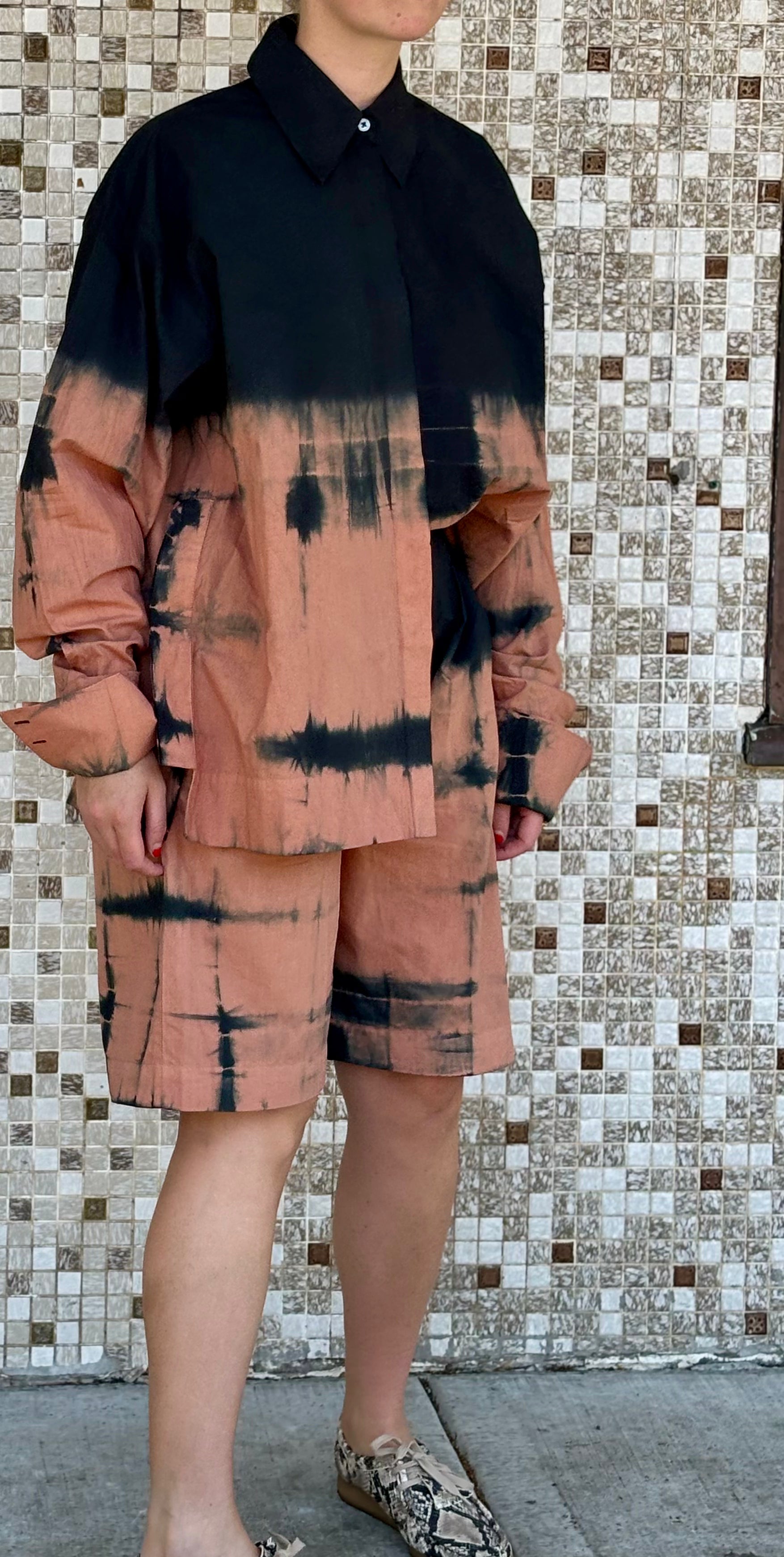 Person wearing a black and pink tie-dye outfit standing against a tiled wall.