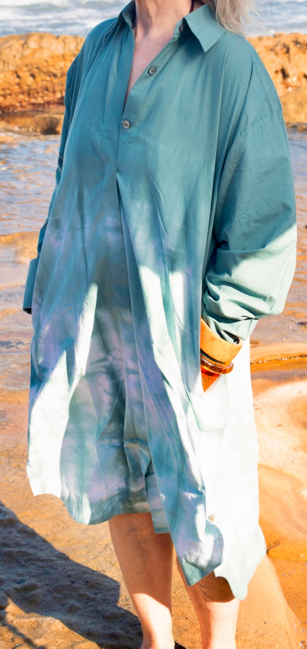 Person wearing a light blue tie-dye shirt dress on a beach